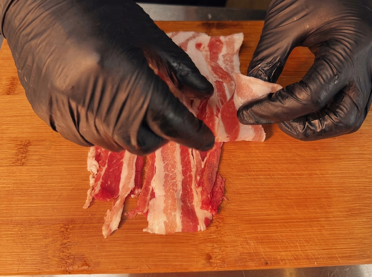 Overlapping slices of raw pork belly prepared for the rolling process.