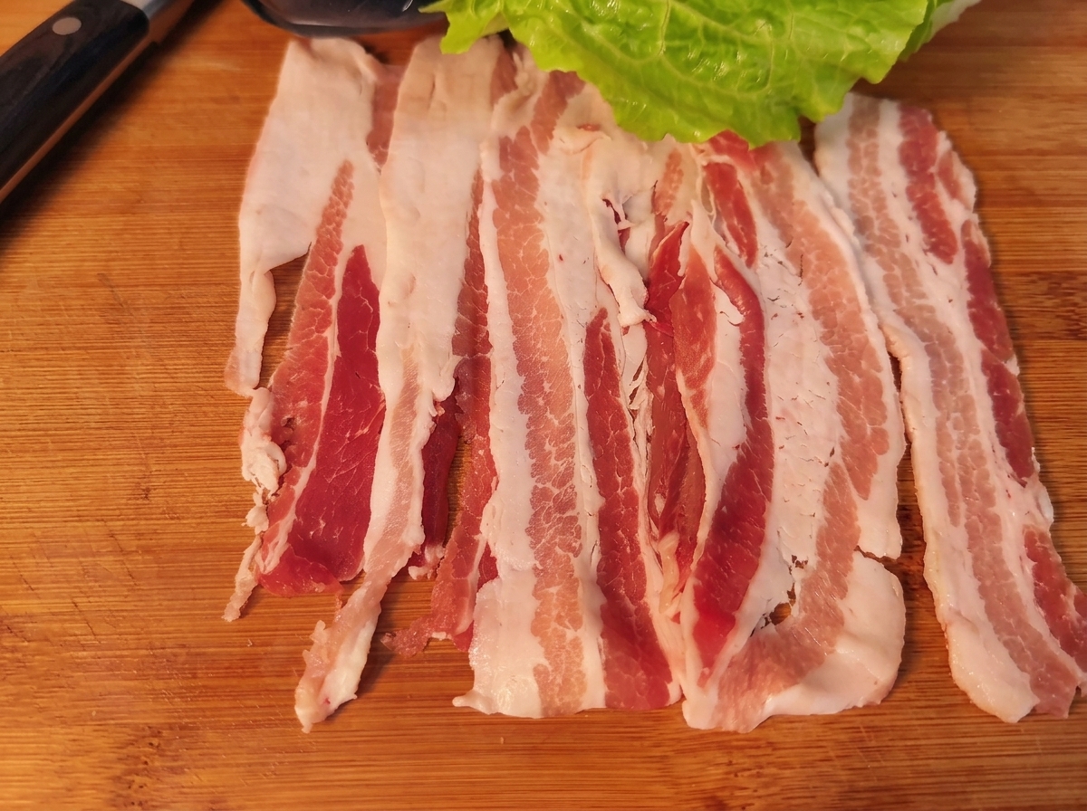 A pork belly slice topped with a lettuce leaf, carrot, onion, and kimchi, ready to be rolled.