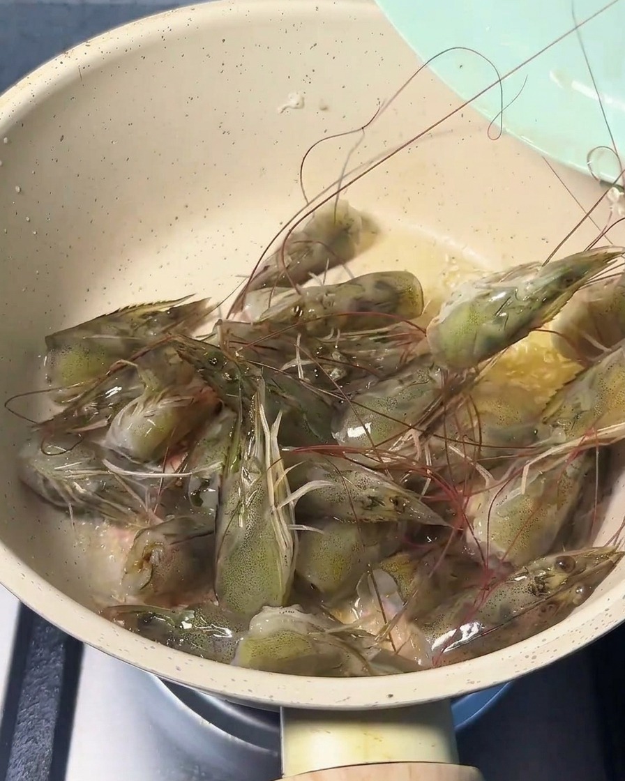 Fresh shrimp heads sizzling in a pan with oil, turning pink and releasing their aroma.
