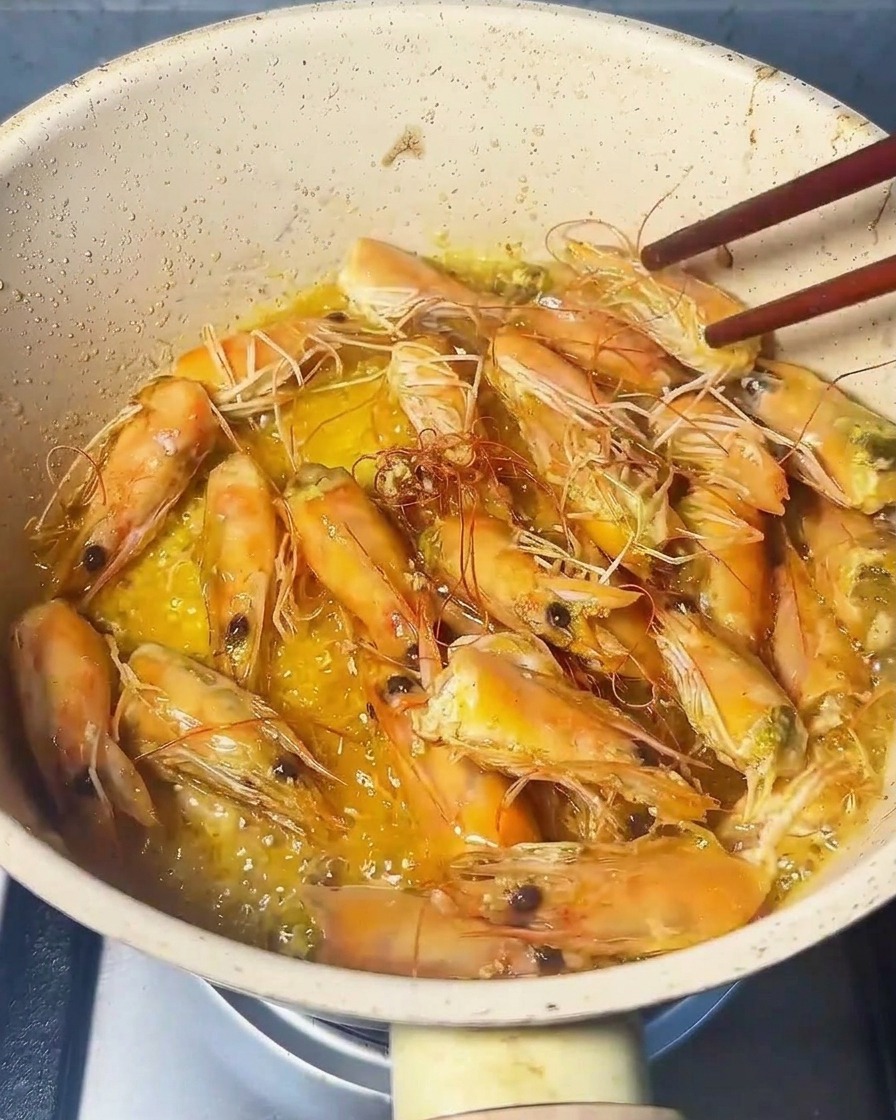 A close-up of shrimp heads being pressed with a spatula in a pan, releasing orange-tinted oil.