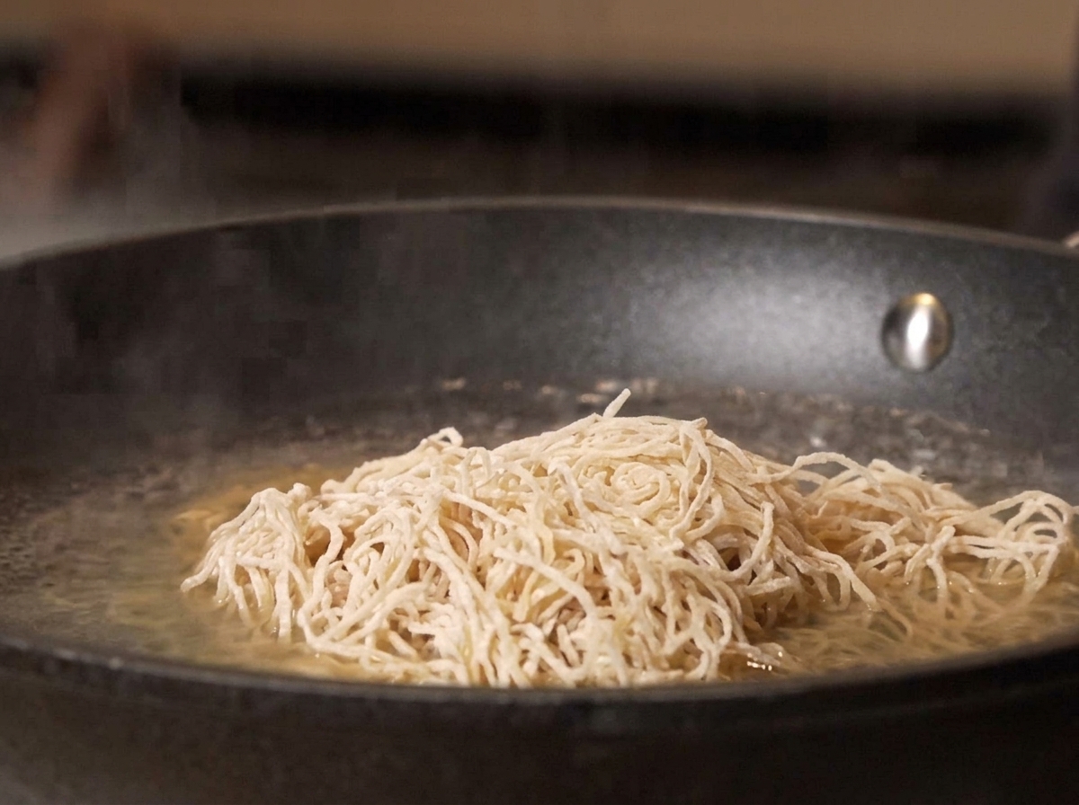 Raw noodles being dropped into a pan of boiling water.
