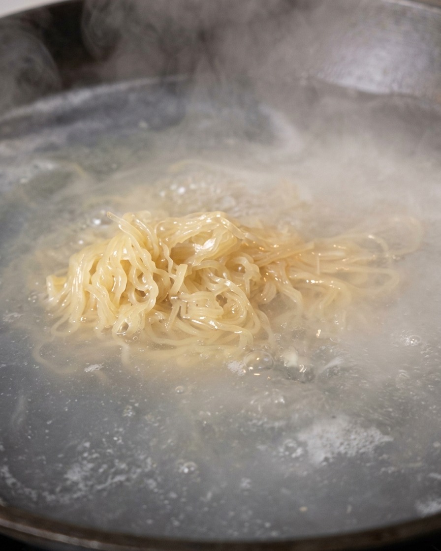 Cooked noodles being lifted out of boiling water to drain.