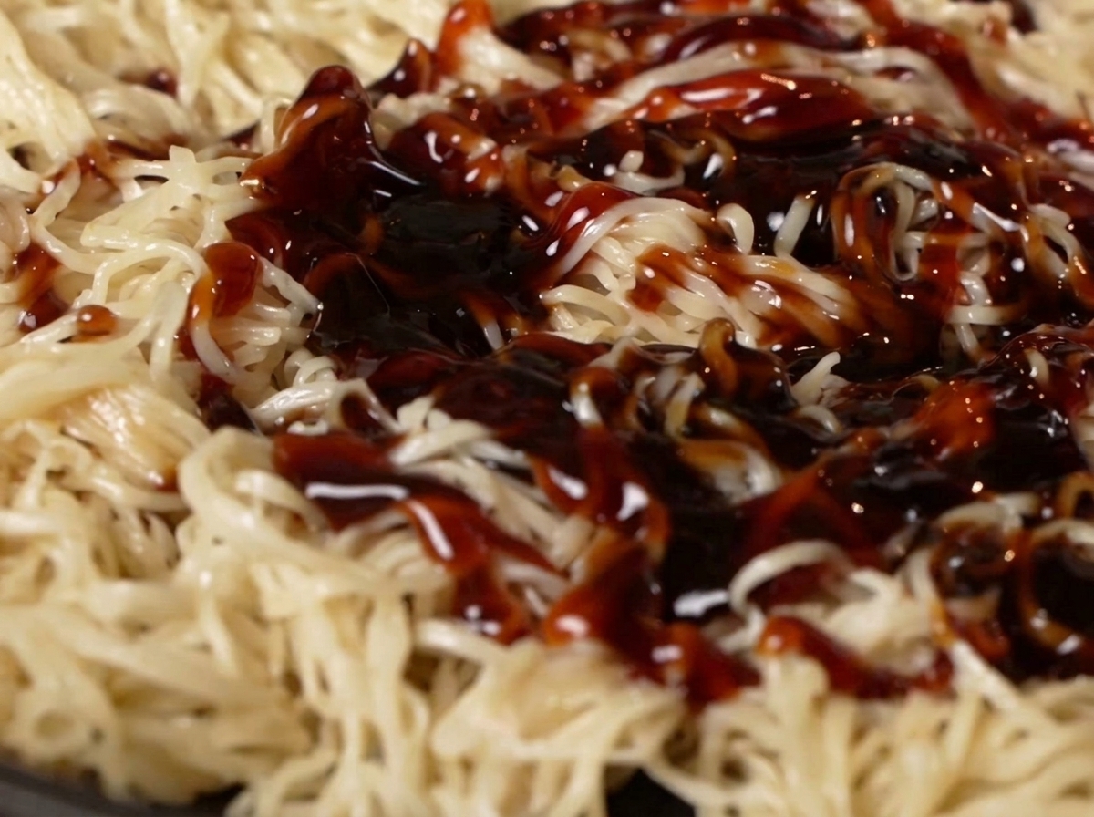 Oyster sauce and soy sauce being poured over noodles in a pan.