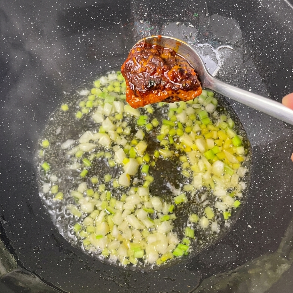 Hot pot base and bean paste being added to the sautéed aromatics in the wok.