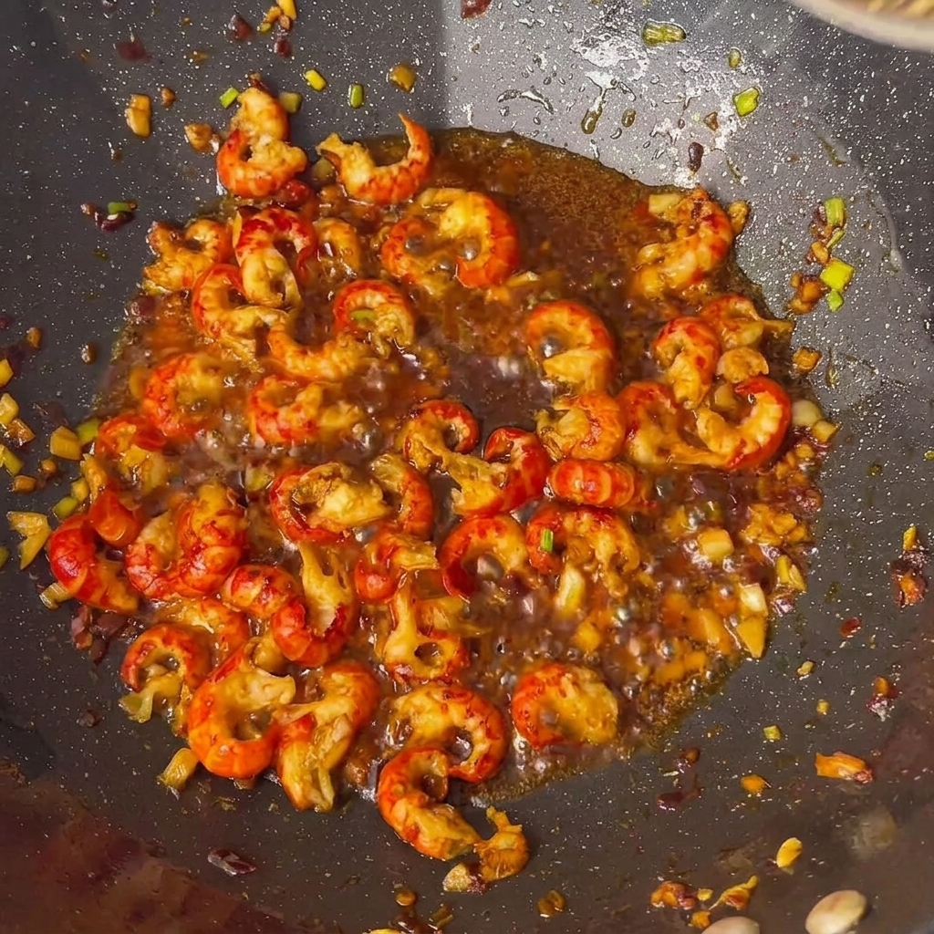 Crawfish tails being seasoned with various sauces and spices in a wok.