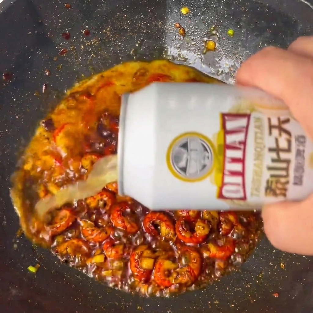 Beer being poured into the wok with the seasoned crawfish tails.