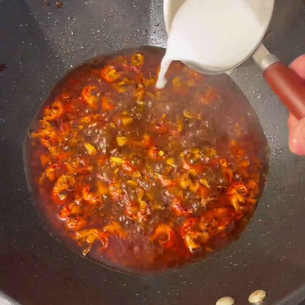A close-up of a cornstarch slurry being poured into a bubbling, savory crawfish sauce in a wok.