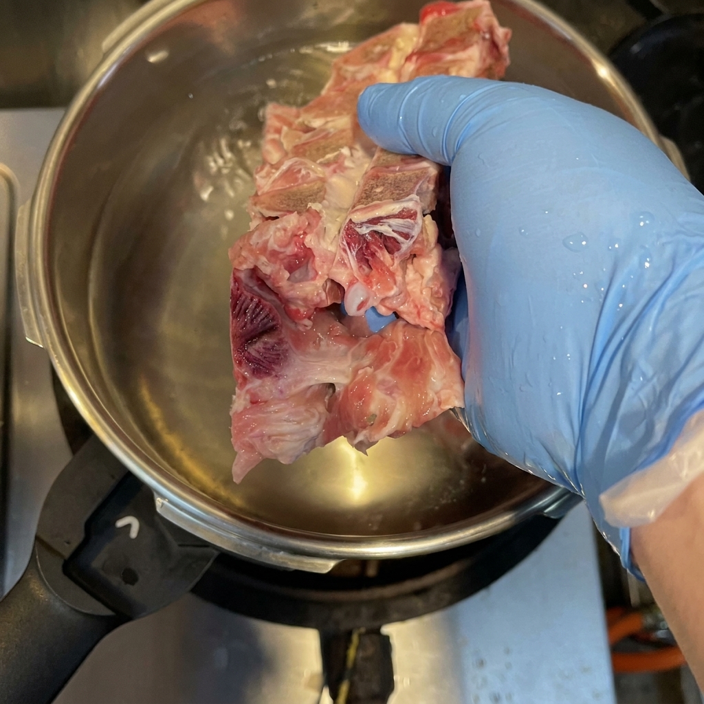 Pork bones, chicken carcass, and pig trotters boiling in a pressure cooker to remove impurities.