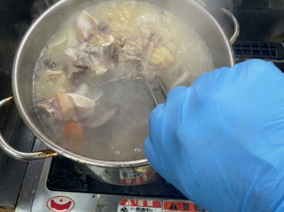 Vigorous stirring of a bubbling, creamy broth in a large stainless steel stockpot.
