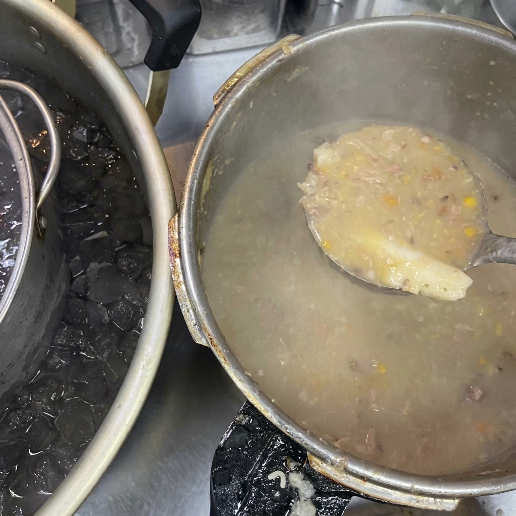 A ladle holding thick, cloudy broth next to a large pot that is sitting in an ice bath.