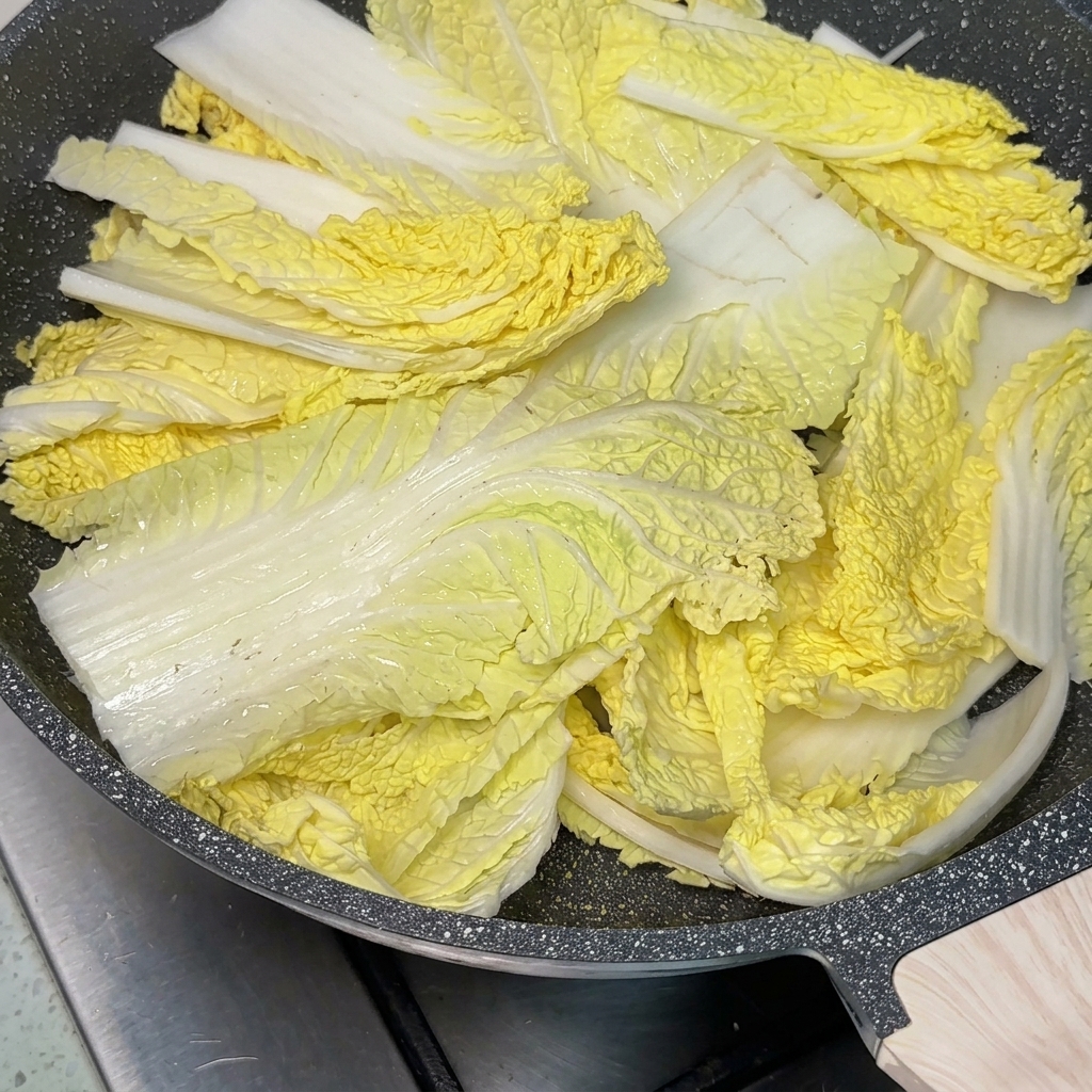 A pan filled with various stew ingredients with a large spoonful of red chili paste in the center, being filled with savory broth.