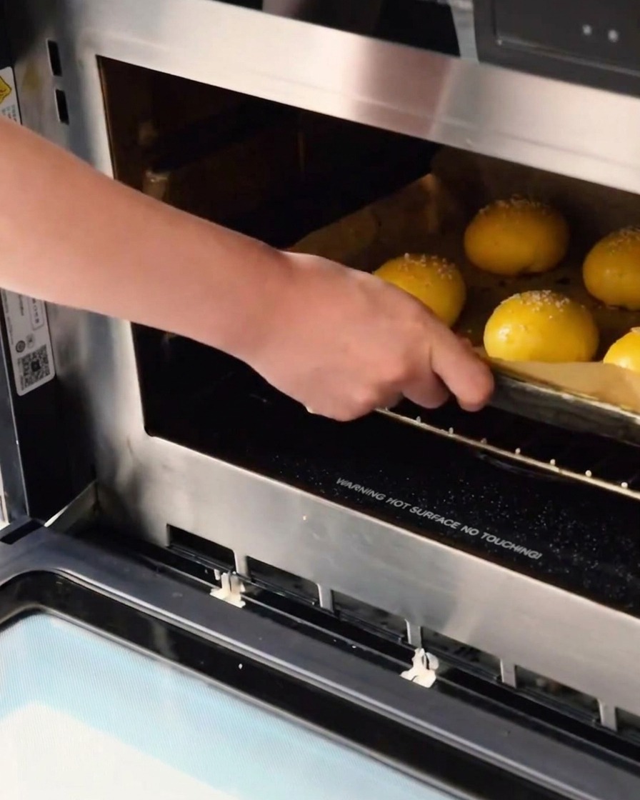 Tray of raw, sesame-topped dough balls being slid into an oven for baking.