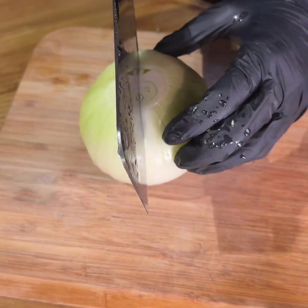 Onions being carefully sliced into consistent strips on a wooden cutting board.