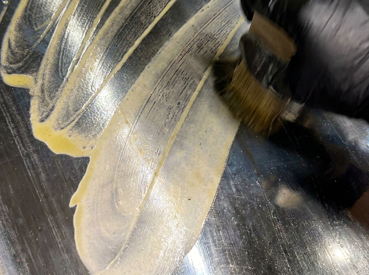 A pastry brush applying melted butter over a clean, preheated flat-top grill surface.