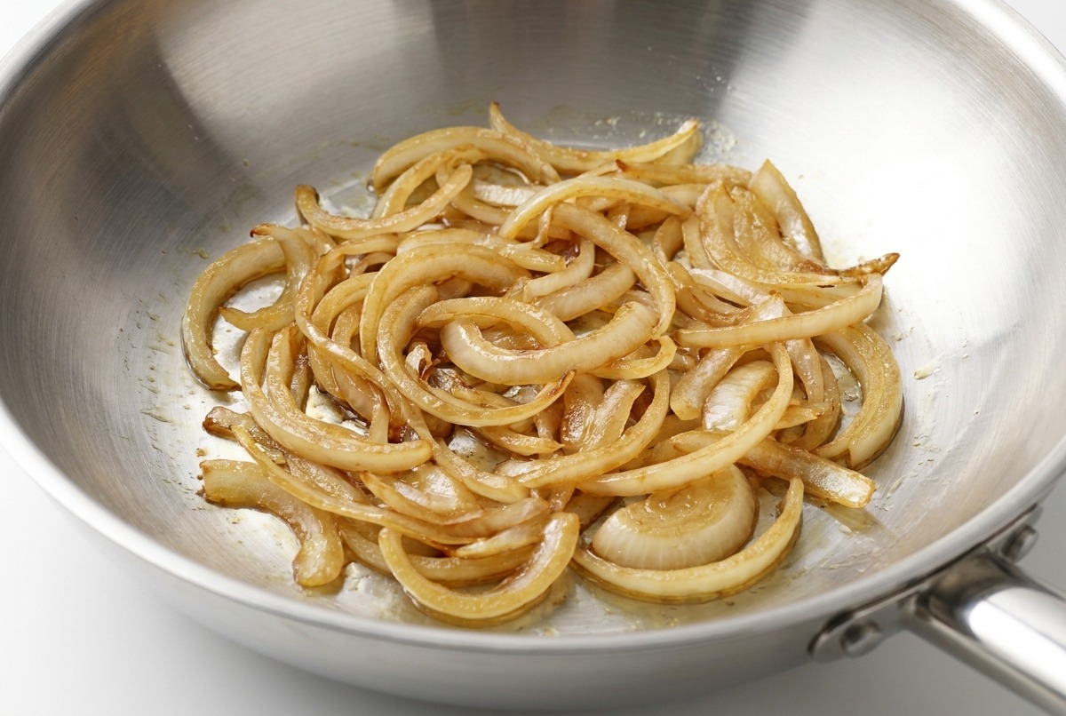 Freshly ground black pepper being seasoned over sautéed onions on a cooking surface.