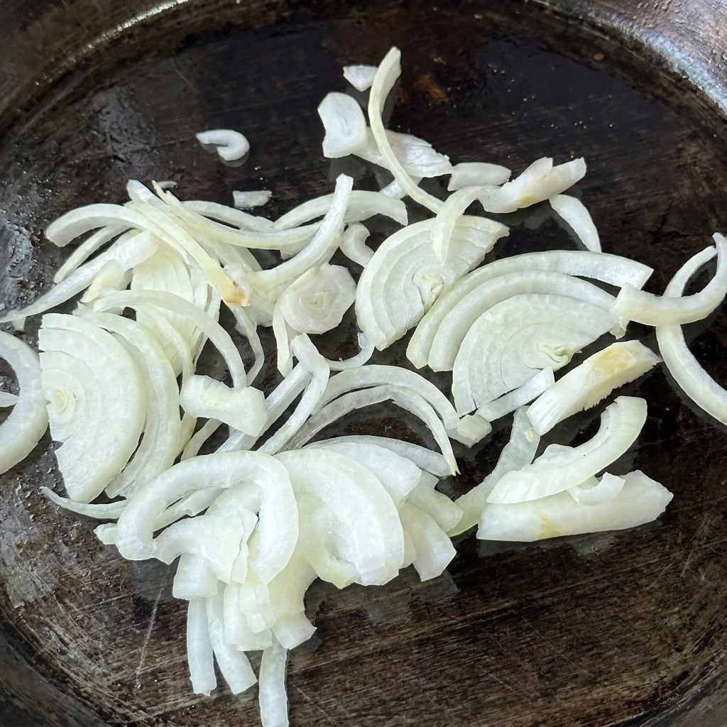A pile of raw, thinly sliced white onions placed onto a greased, dark flat-top cooking griddle.
