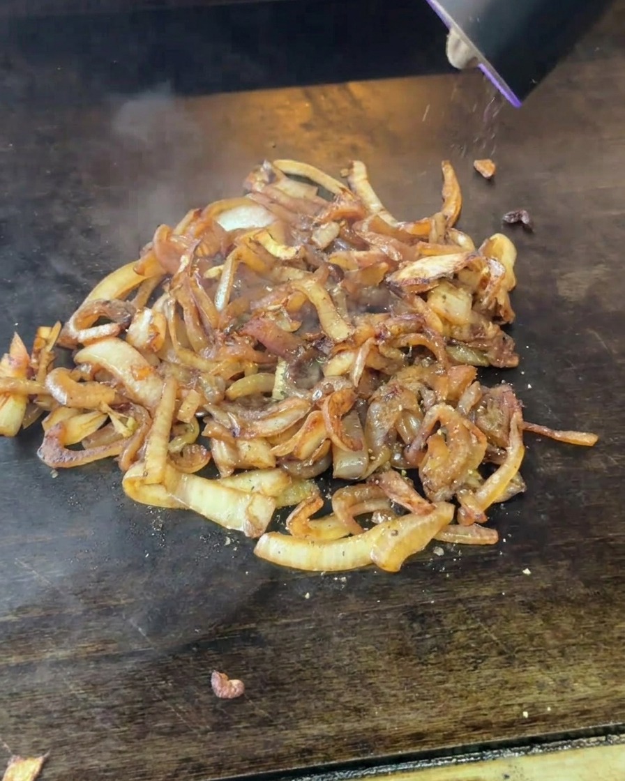 An electric grinder dispensing freshly ground black pepper onto a mound of soft, browned onions.