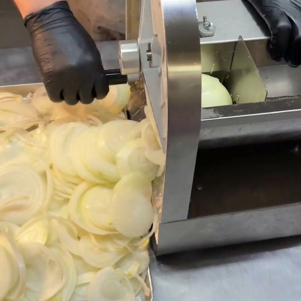 A pile of freshly sliced white onions sitting next to a stainless steel mechanical slicer.
