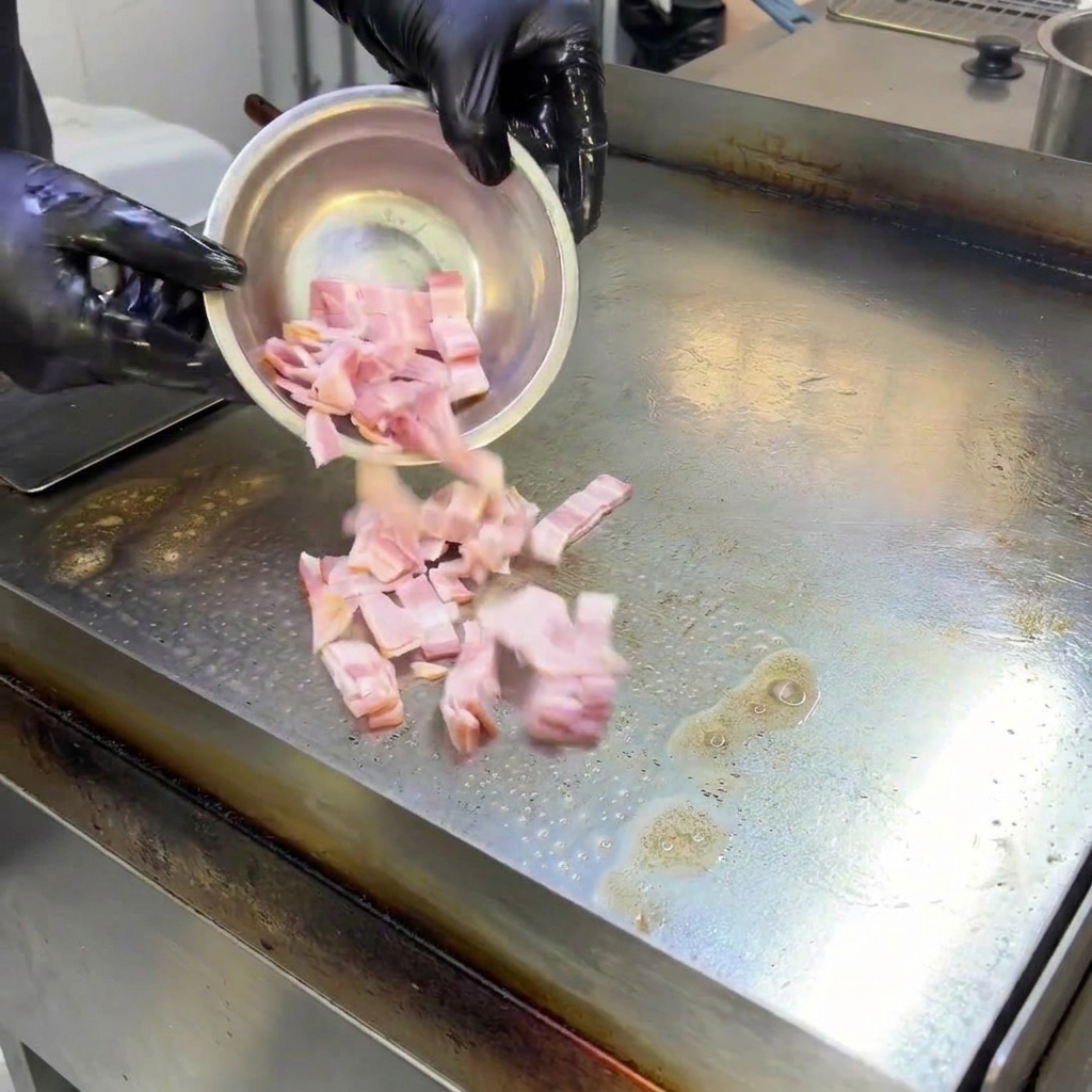 Pieces of bacon sizzling and frying on a hot flat-top grill surface, releasing rendered fat.