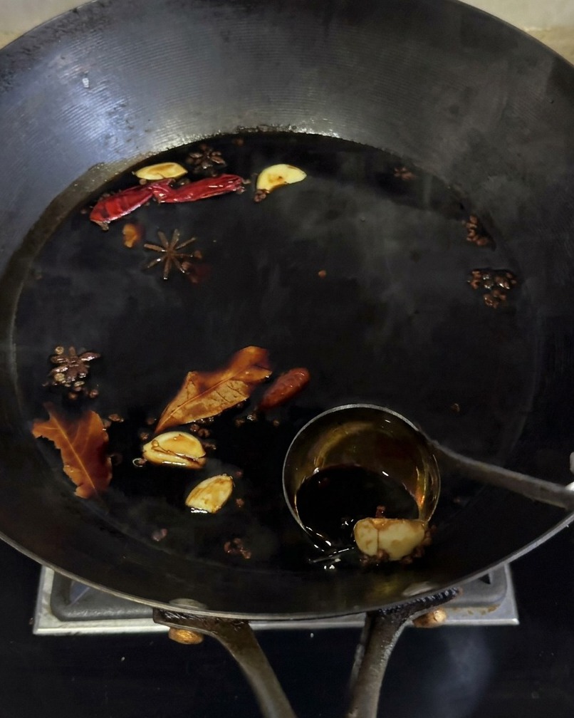 Dark soy sauce marinade simmering in a wok with various aromatics like star anise and garlic.