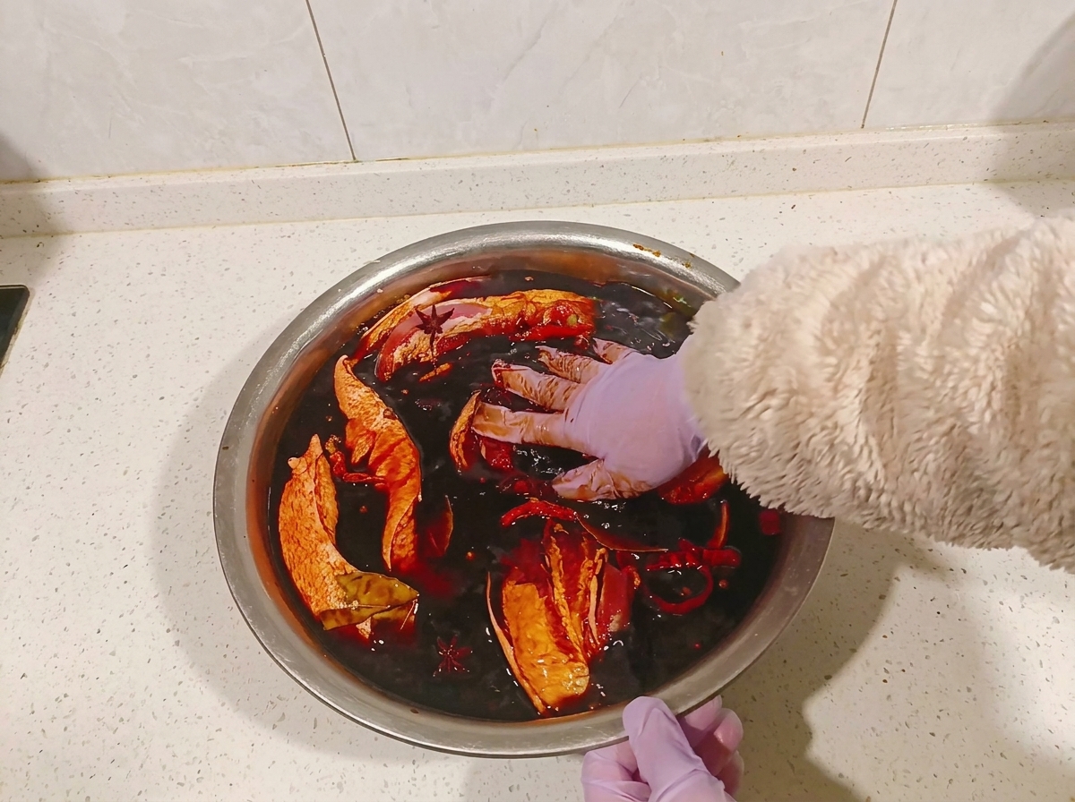 Gloved hands turning pork belly pieces in a bowl of dark soy marinade.