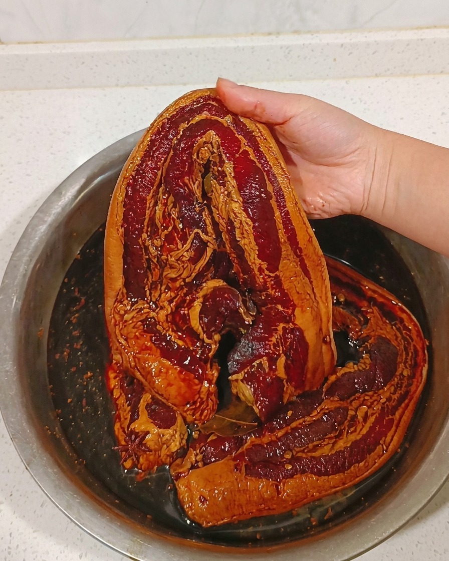 A piece of marinated pork belly being rinsed under a warm stream of water.