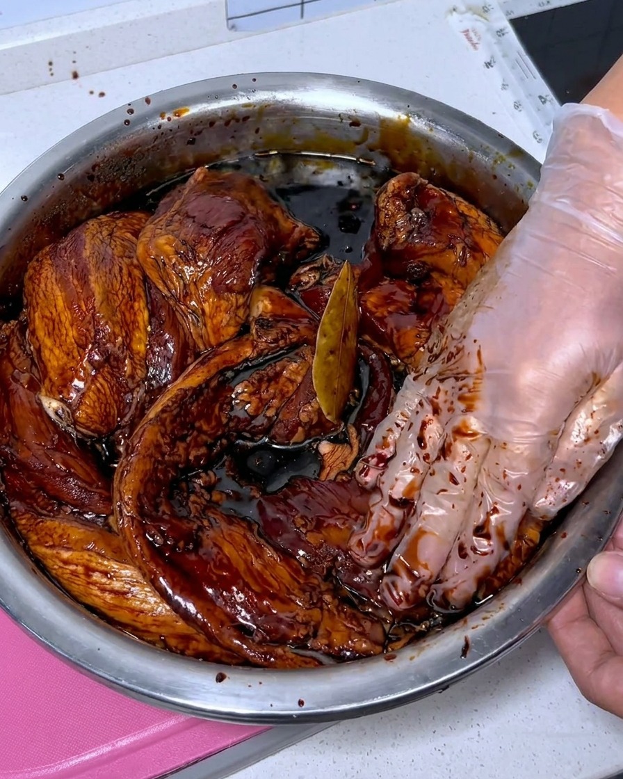Fresh pork belly strips being cleaned with baijiu inside a stainless steel bowl.
