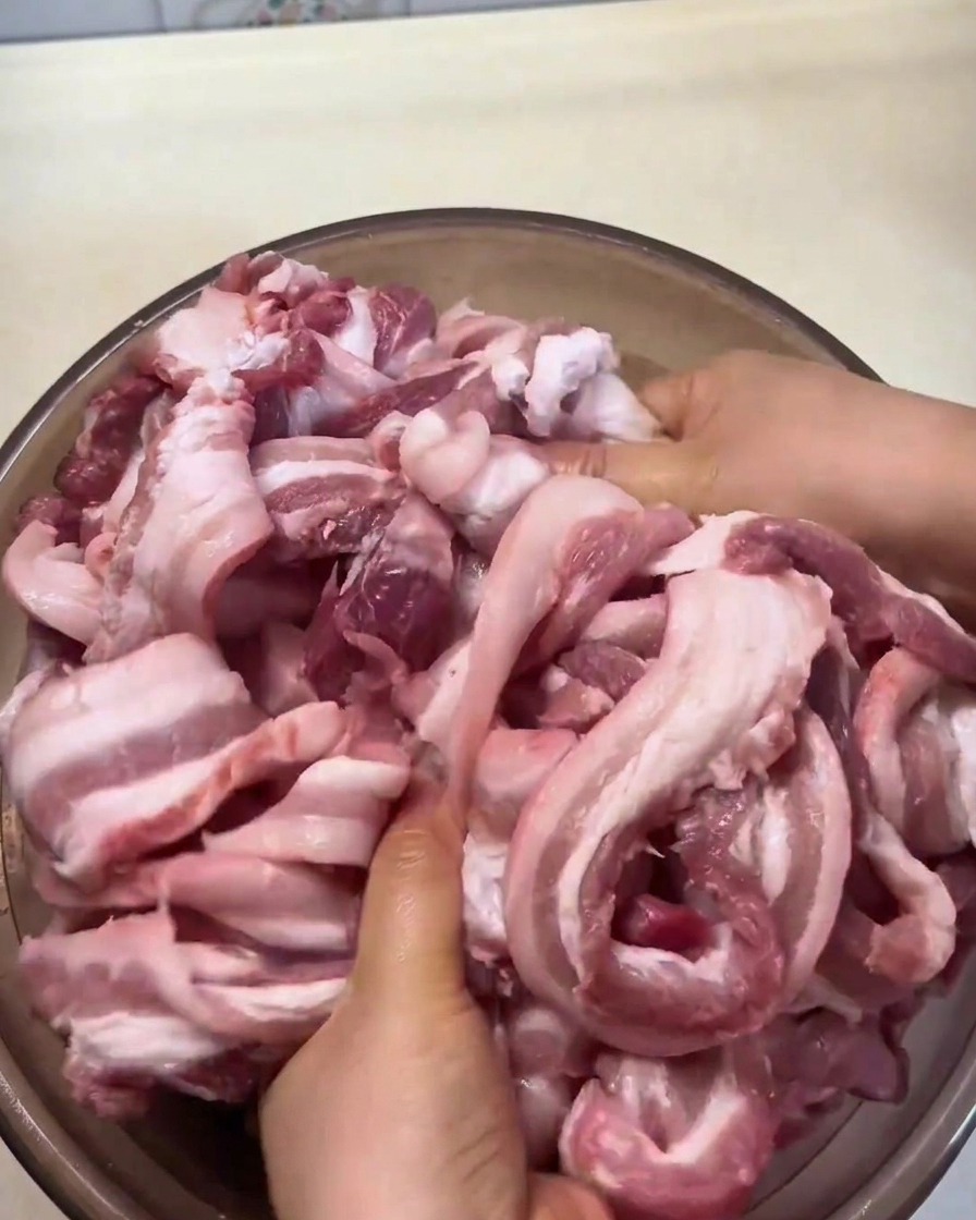 Raw pork belly strips being massaged by hand with spices and seasonings in a large bowl.