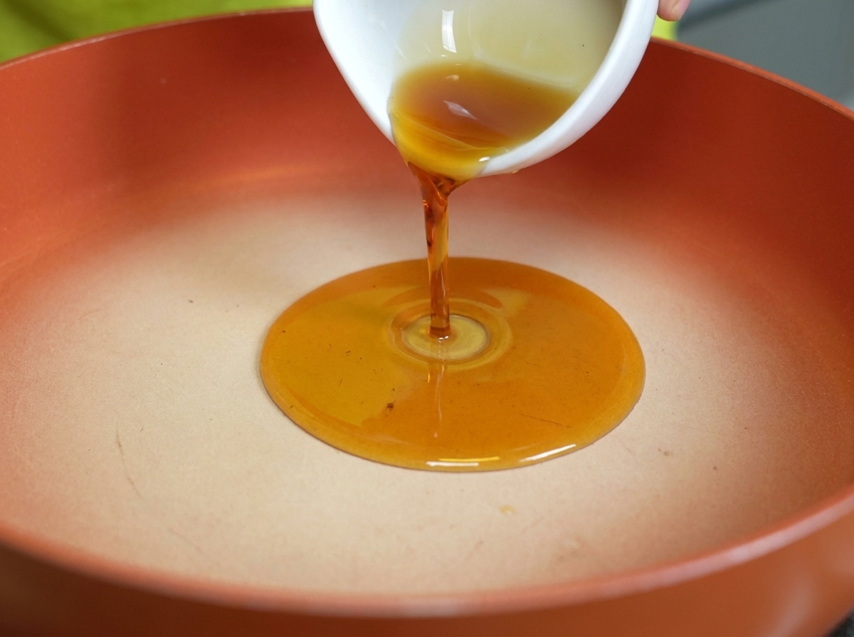 Golden sesame oil being poured into a clean, warm skillet.