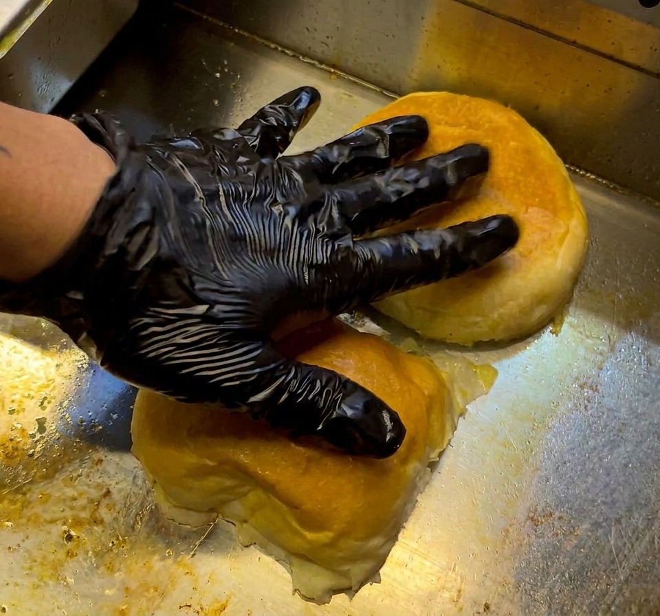 A raw seasoned beef patty placed on a hot, sizzling griddle surface.