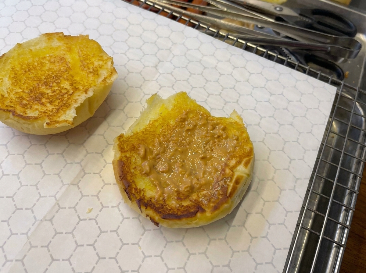 Close-up of a sauce-topped toasted bun being lightly seared with a kitchen blowtorch.