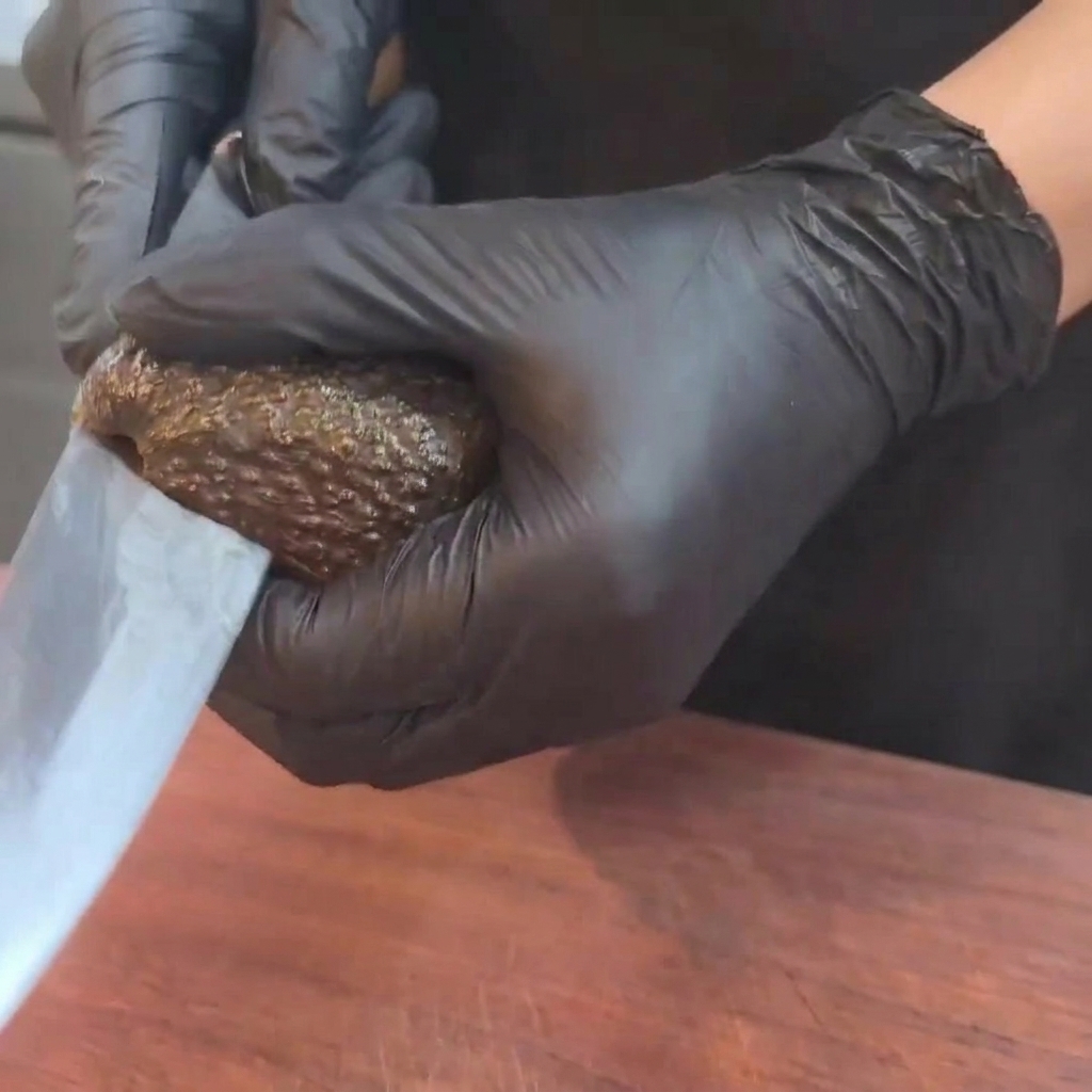A ripe, dark-skinned avocado being cut in half with a sharp knife on a wooden cutting board.