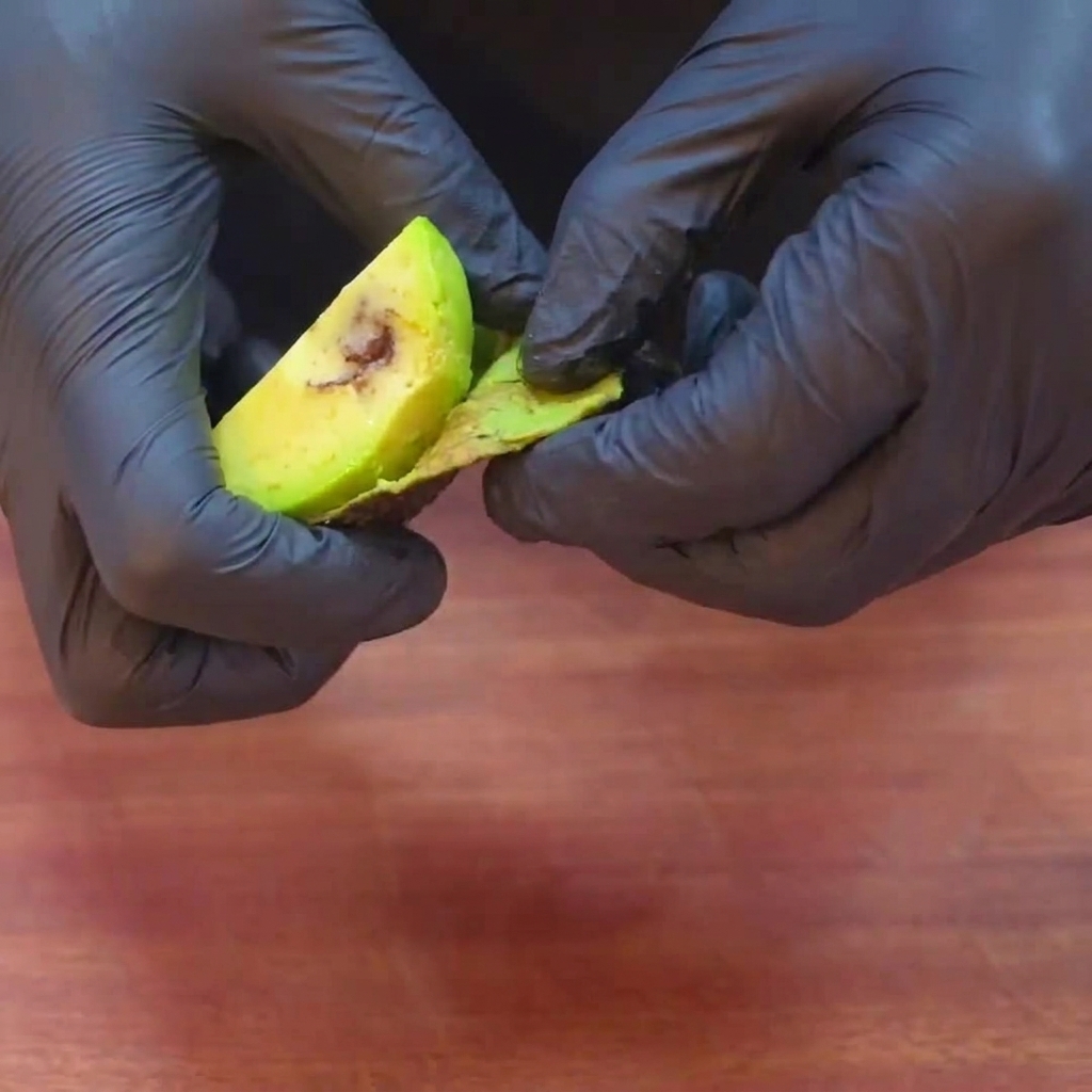 Uniform slices of green avocado being peeled and prepared for the burger assembly.