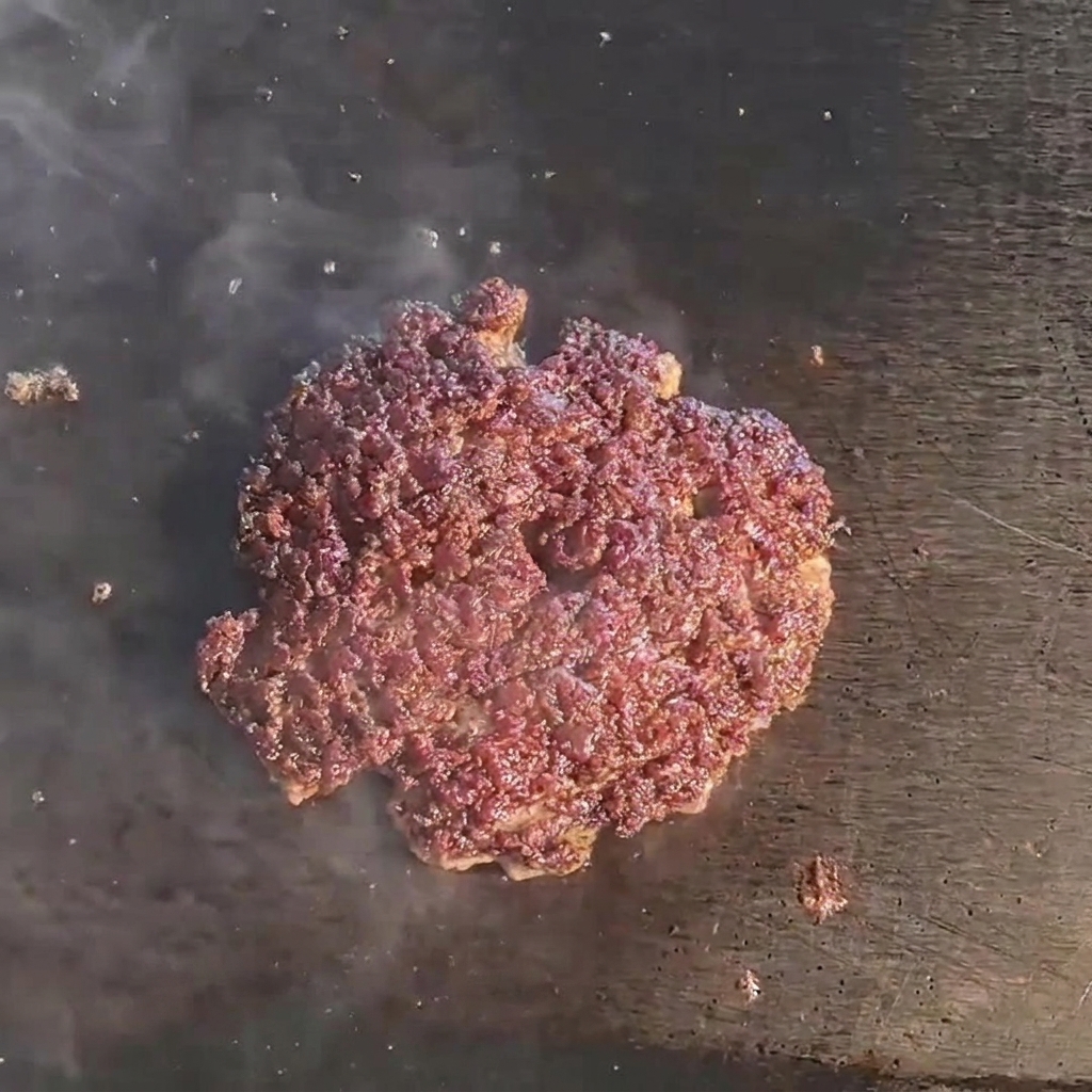 A melting slice of cheese covering a browned, juicy beef patty on a hot grill.