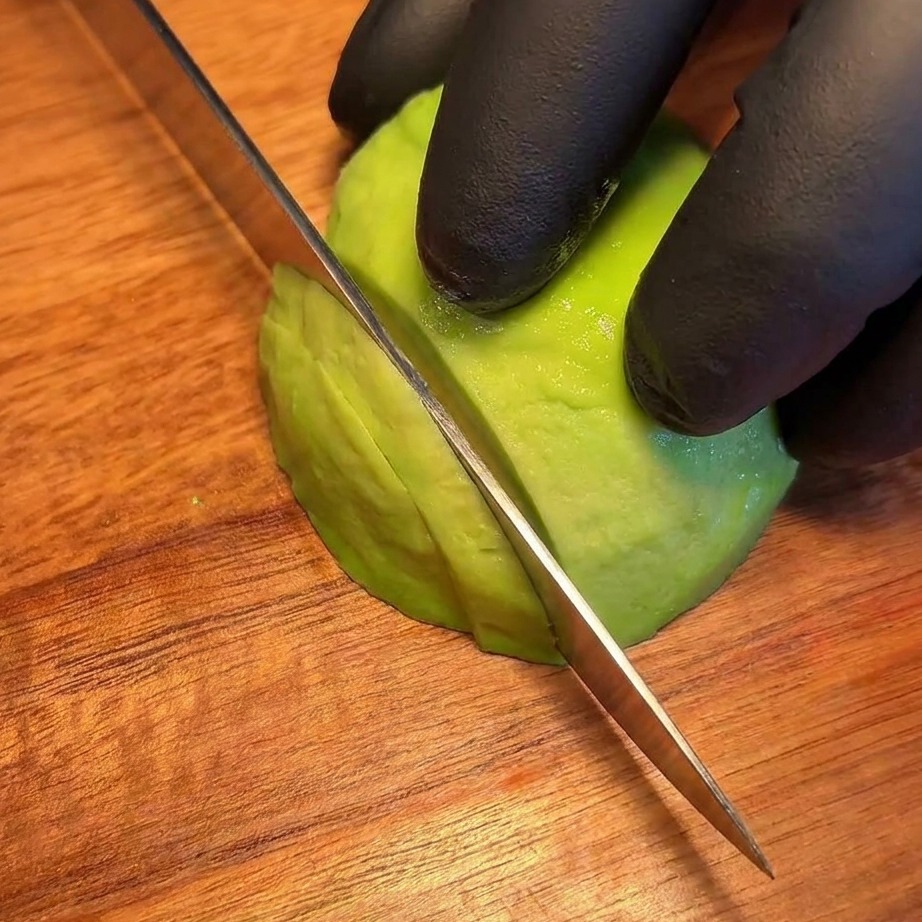 Thin, uniform slices of fresh avocado neatly arranged on a wooden board.