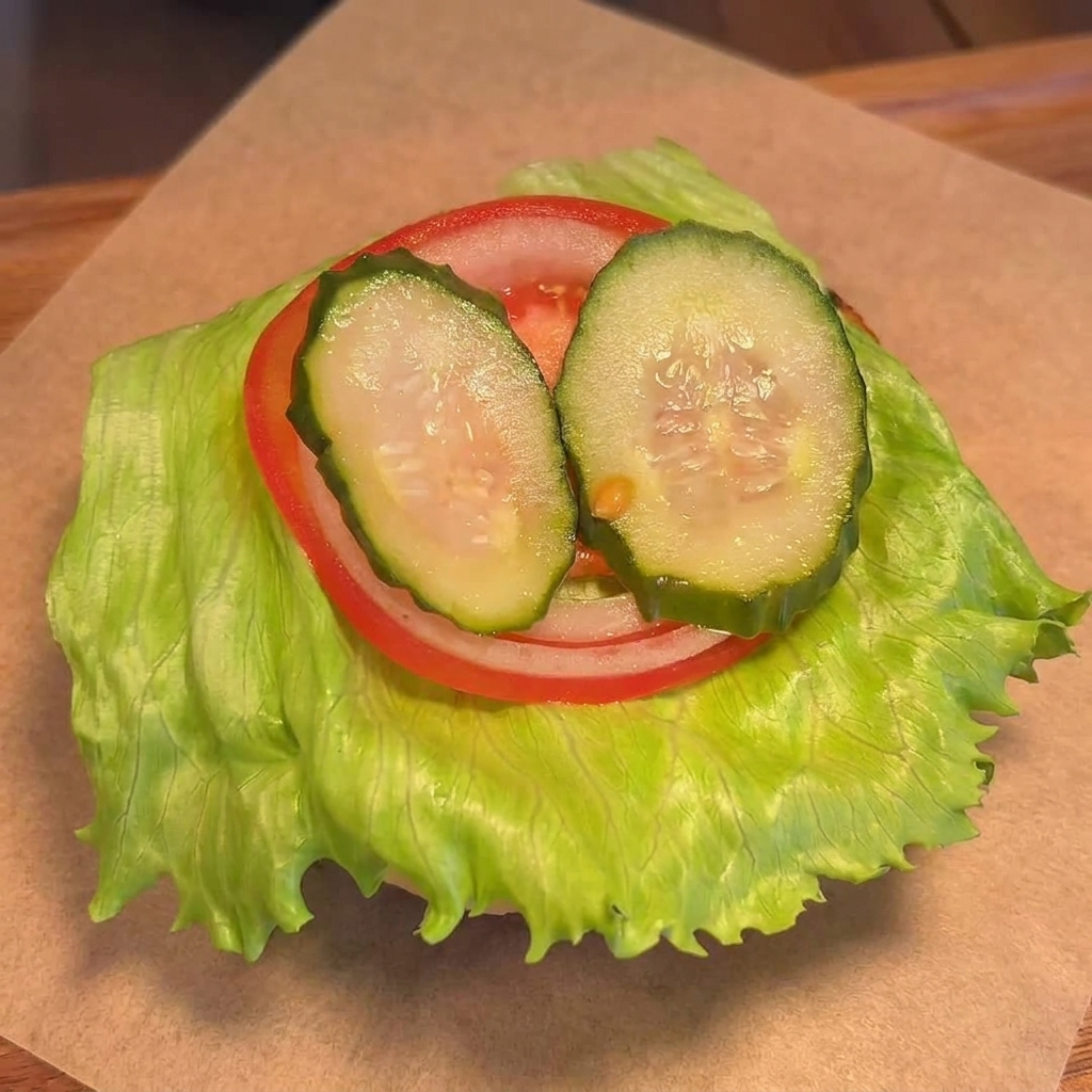 A cooked beef patty with melted yellow cheese being placed onto a bun layered with lettuce, tomato, and pickles.