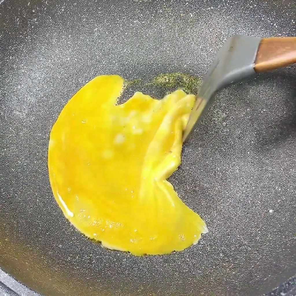 An egg pancake cooking in a pan, with the edges being pulled toward the center.