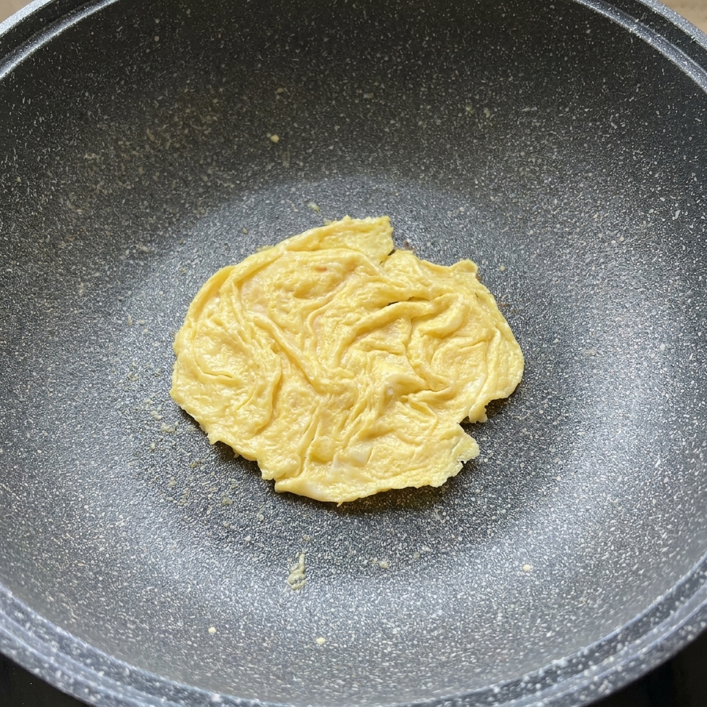 A slice of cheese melting over a cooked egg pancake in a frying pan.