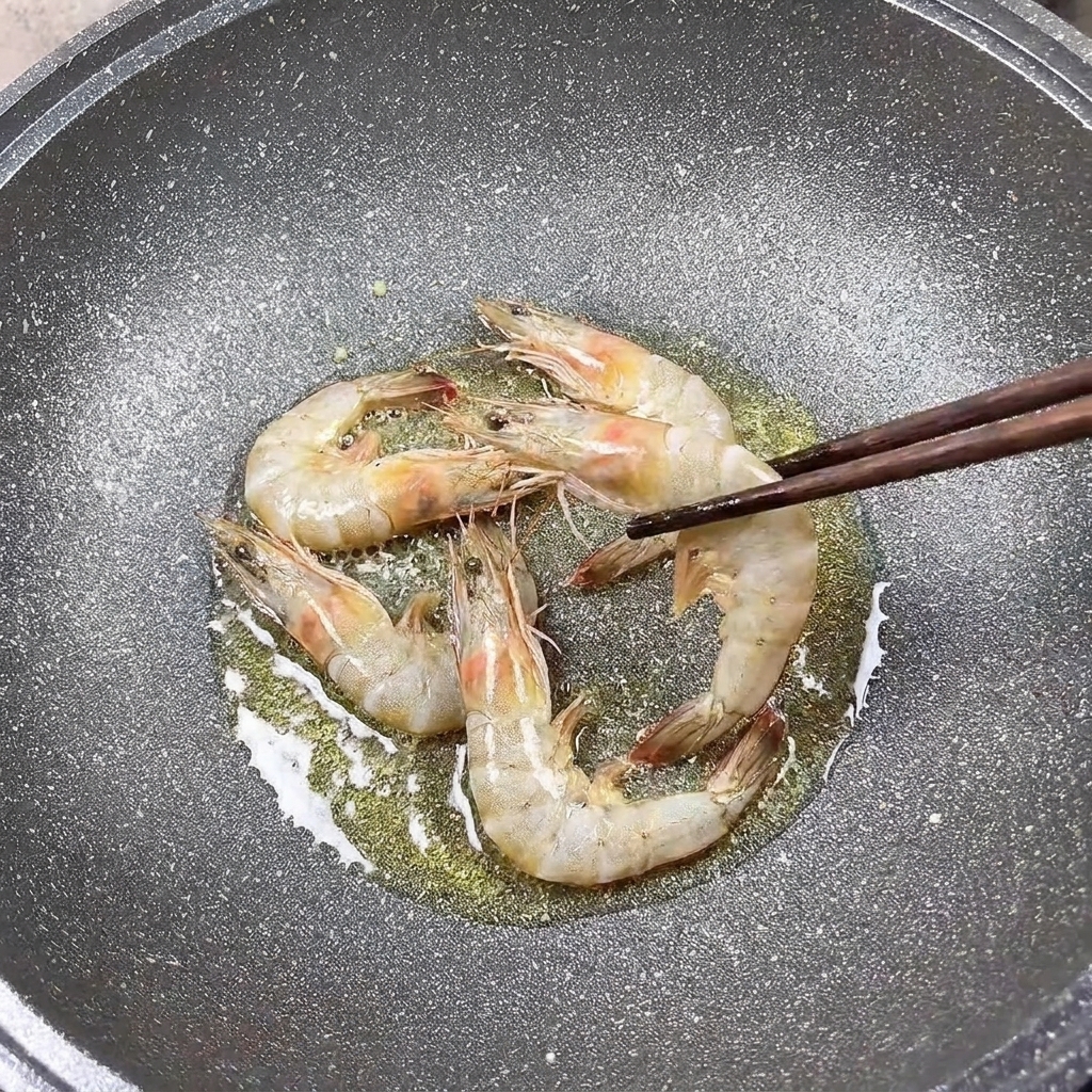 Seasoned prawns frying in a pan, being turned with chopsticks.