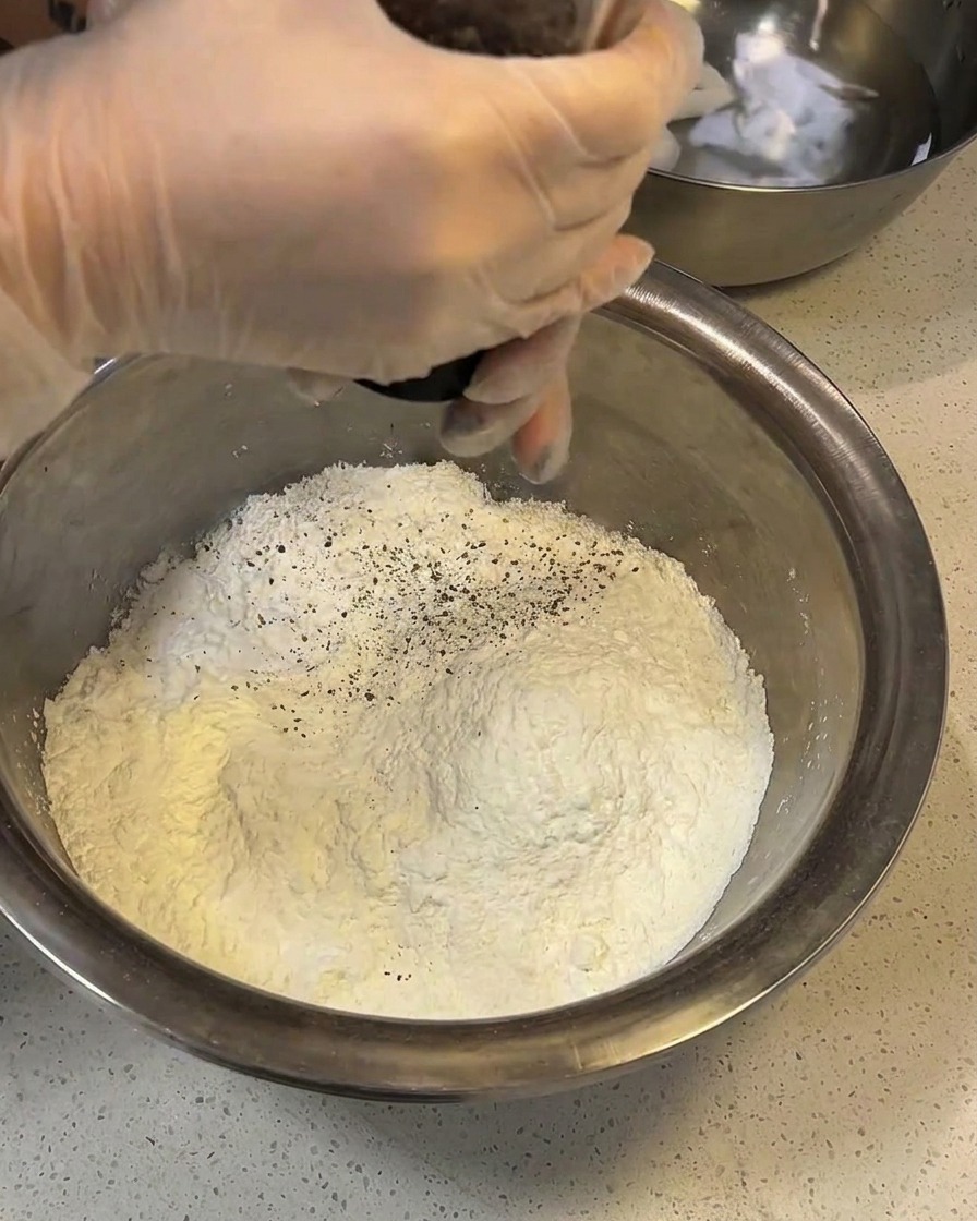 Flour, cornstarch, and spices being mixed together in a large stainless steel bowl.