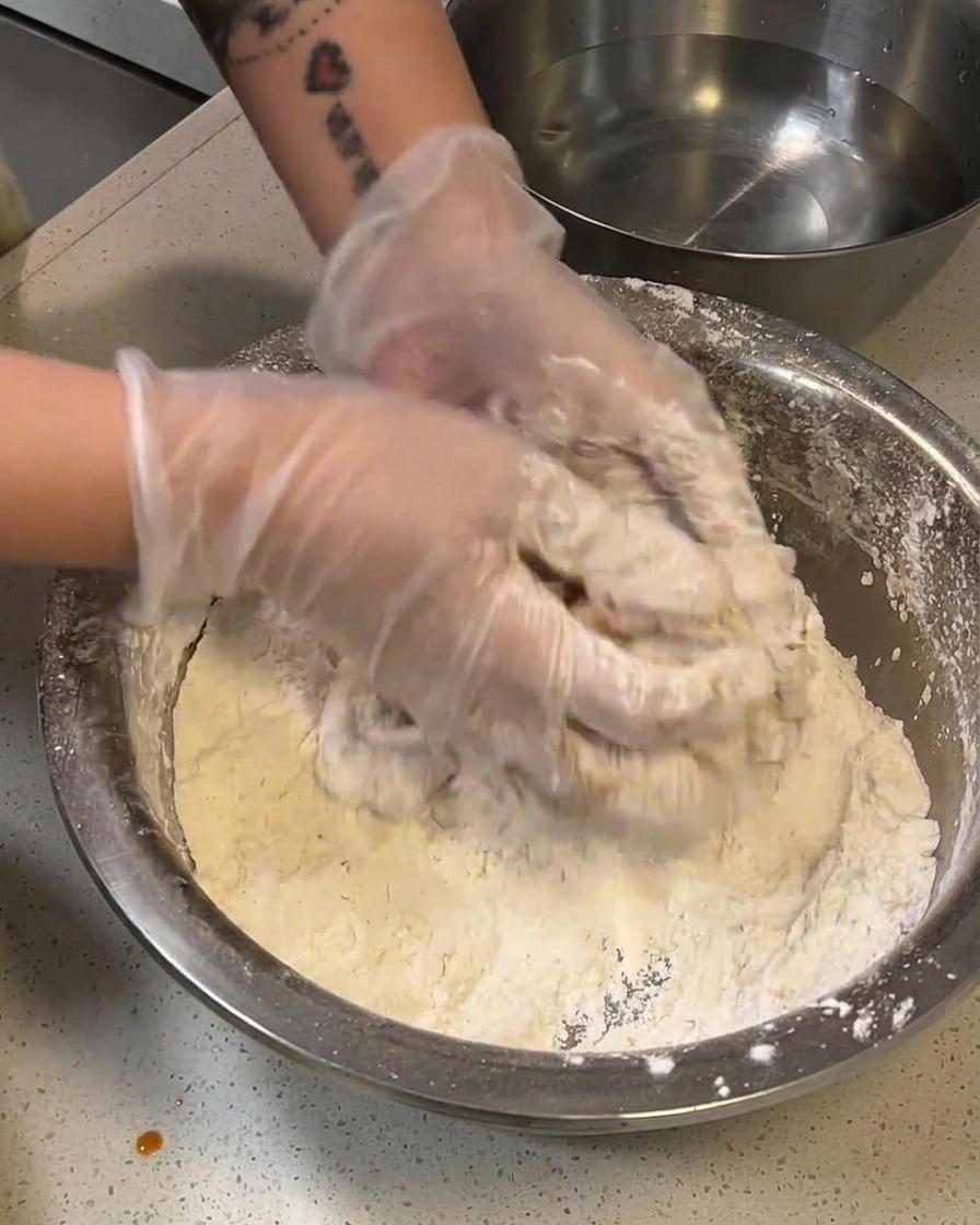 A flour-coated chicken thigh being dipped briefly into a bowl of water.
