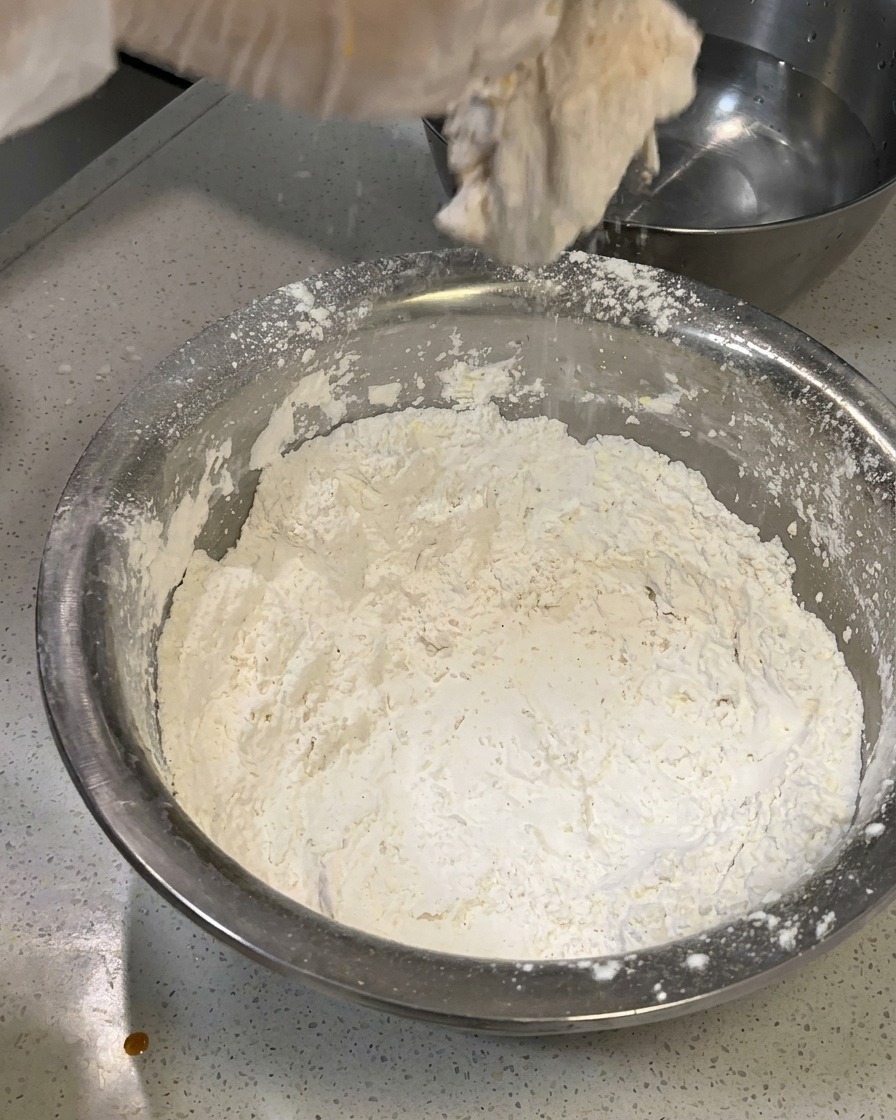 The breaded chicken thigh being gently coated with more flour to create a flaky, textured crust.