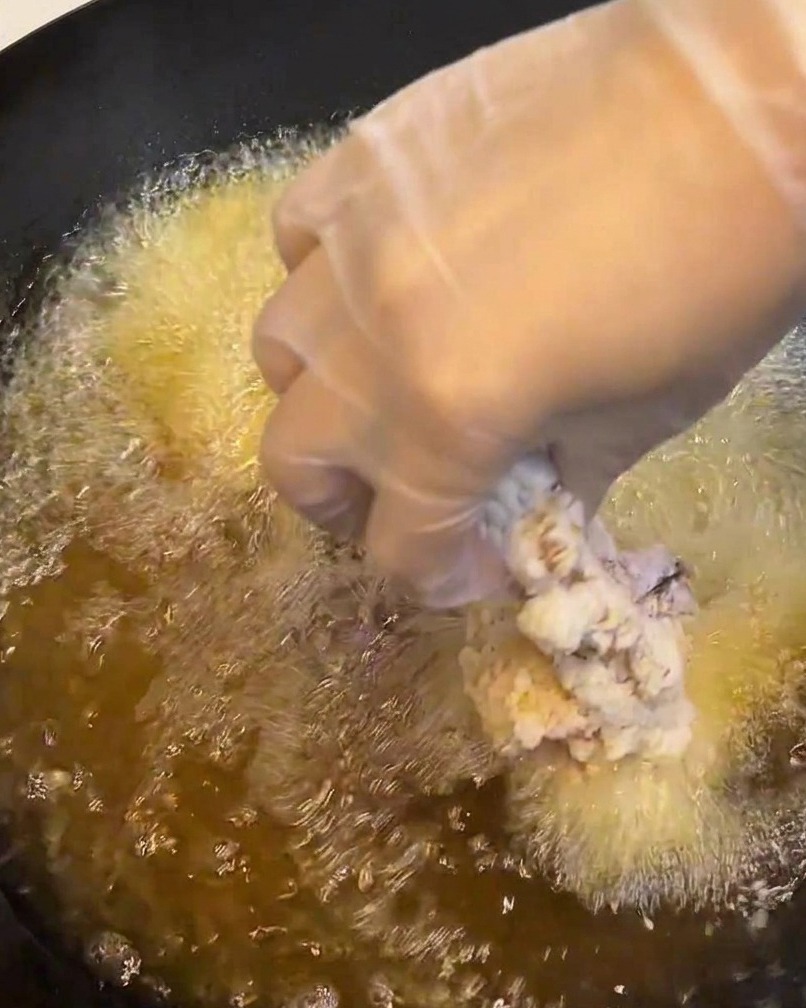 A breaded chicken thigh being lowered into a pan of hot, bubbling oil.