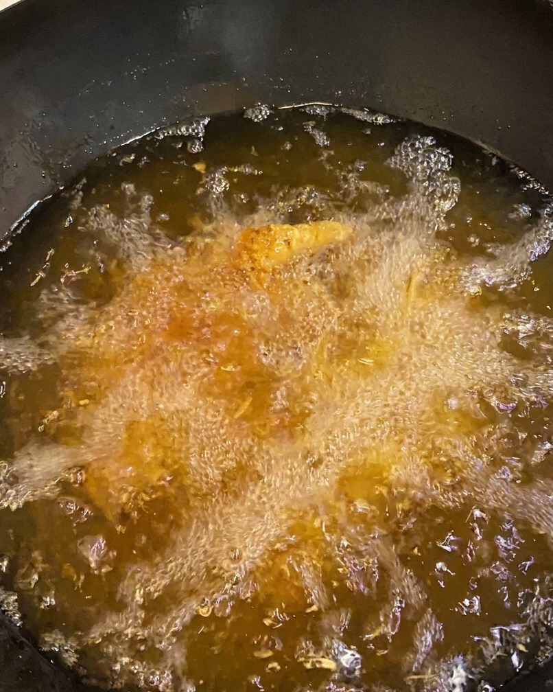 Chicken thighs frying in deep oil, showing a deep golden-brown crust.