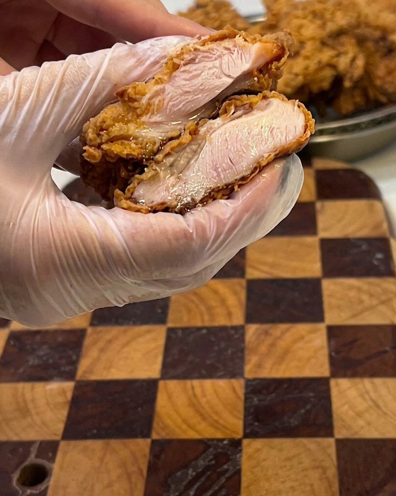 A close-up of a fried chicken fillet cut open, showing the moist, white meat inside.
