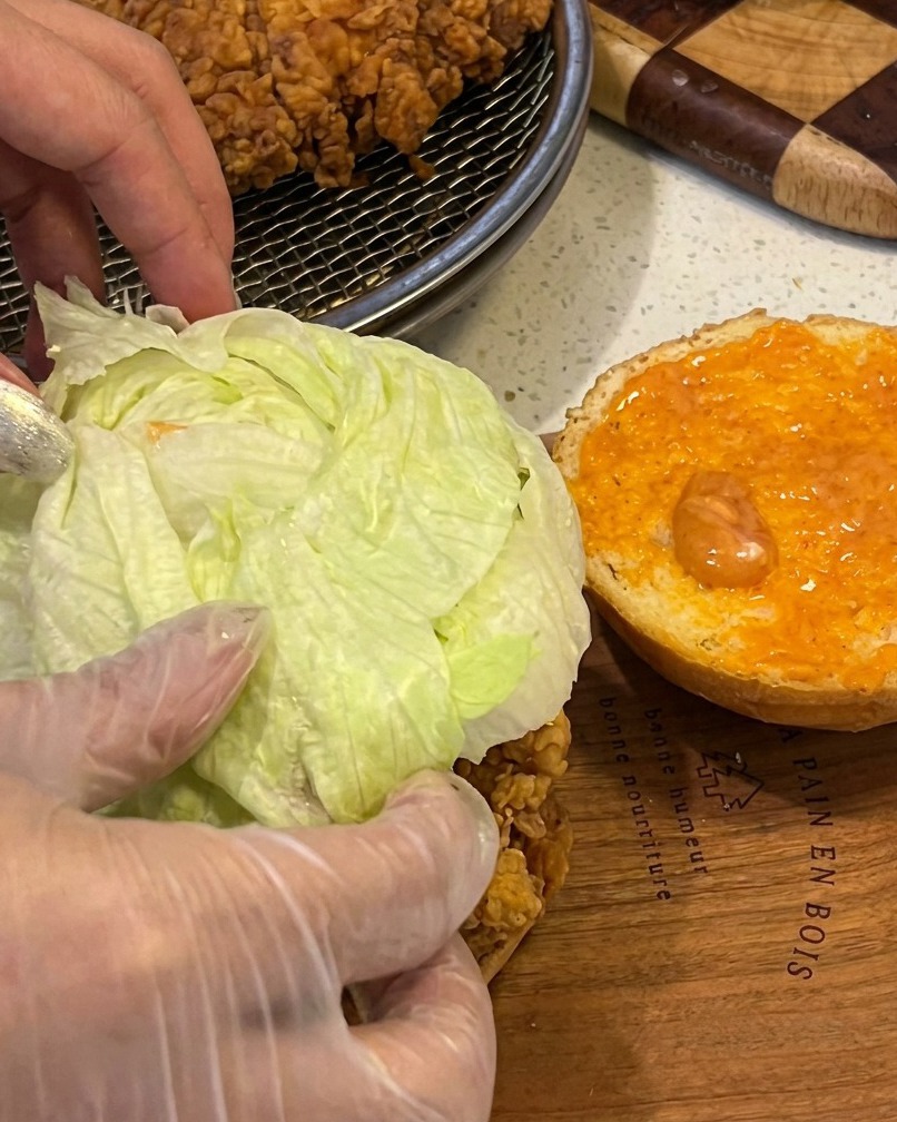 Assembling a chicken burger with a crispy fillet, fresh lettuce, and sauce on a toasted bun.