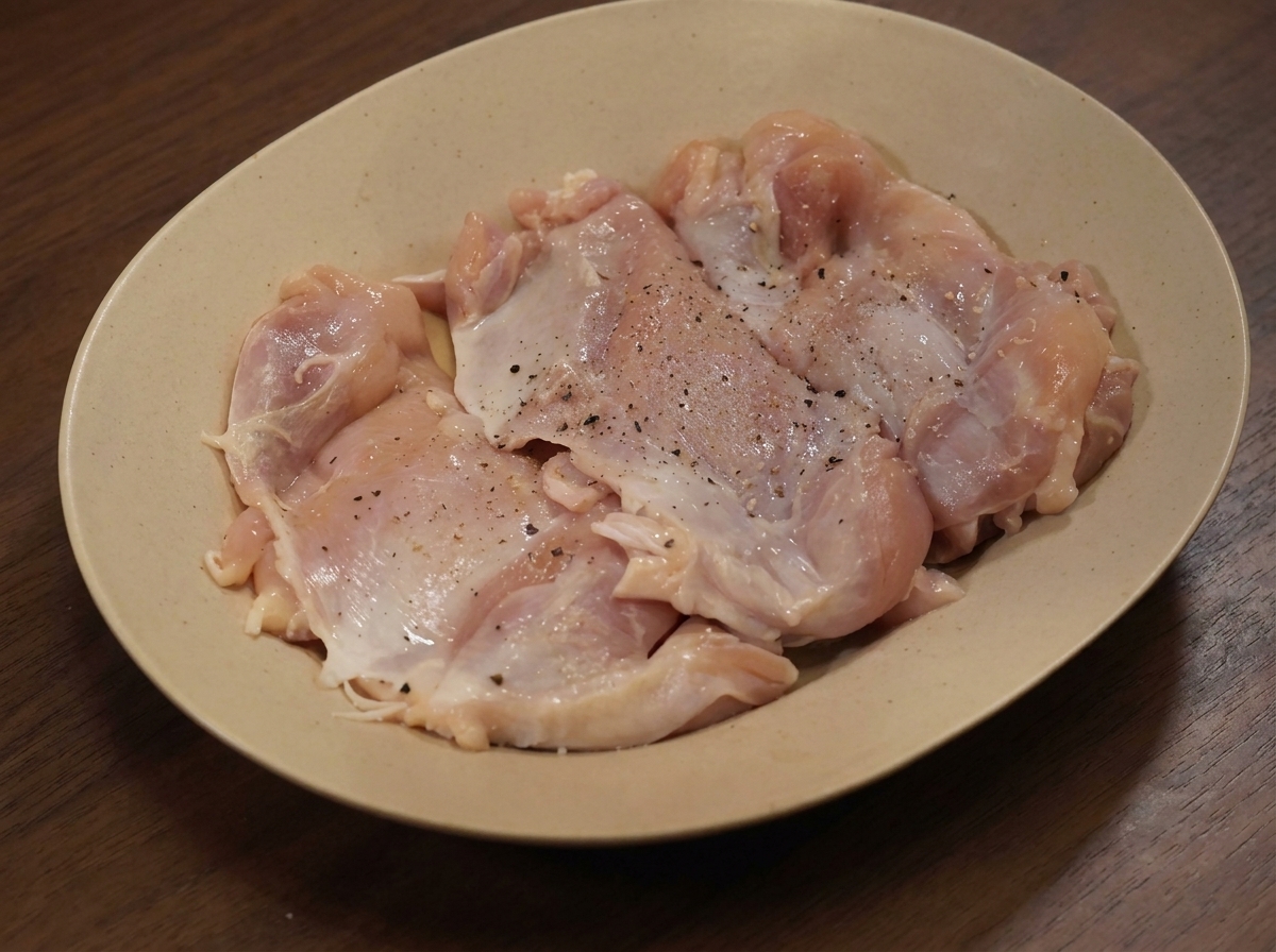 Raw chicken thighs on a plate sprinkled with various dry seasonings.