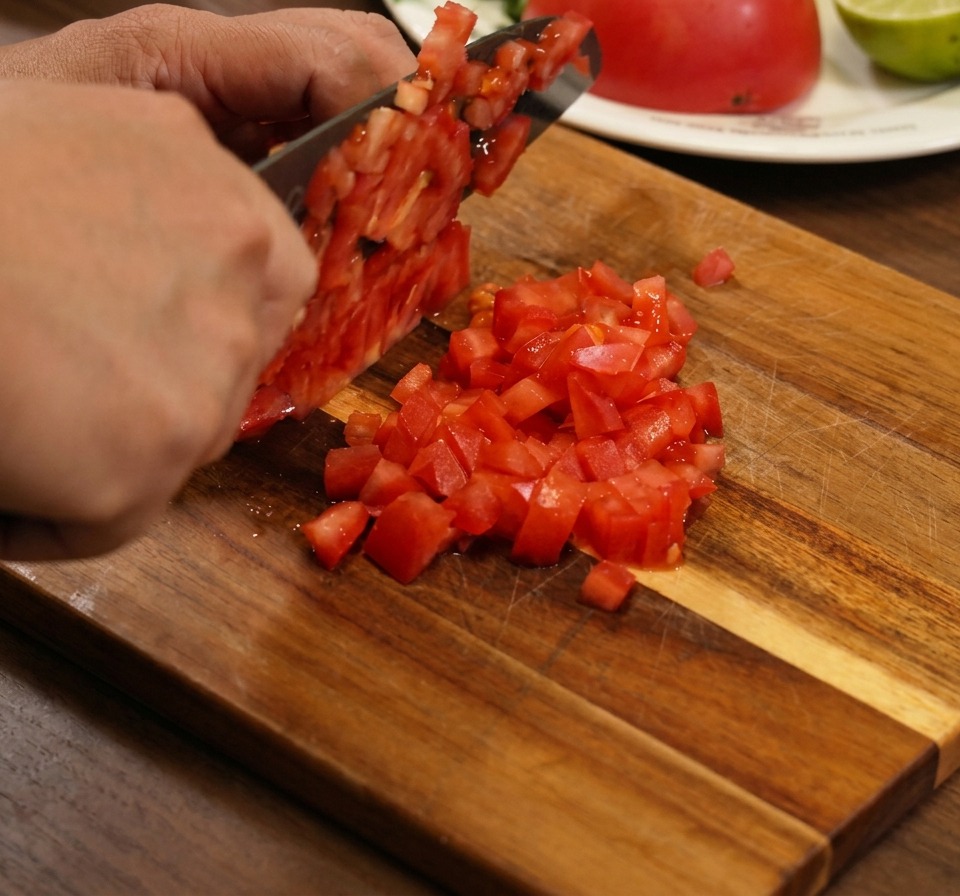 A close-up of fresh, diced tomatoes, red onions, and cilantro being tossed together in a bowl.
