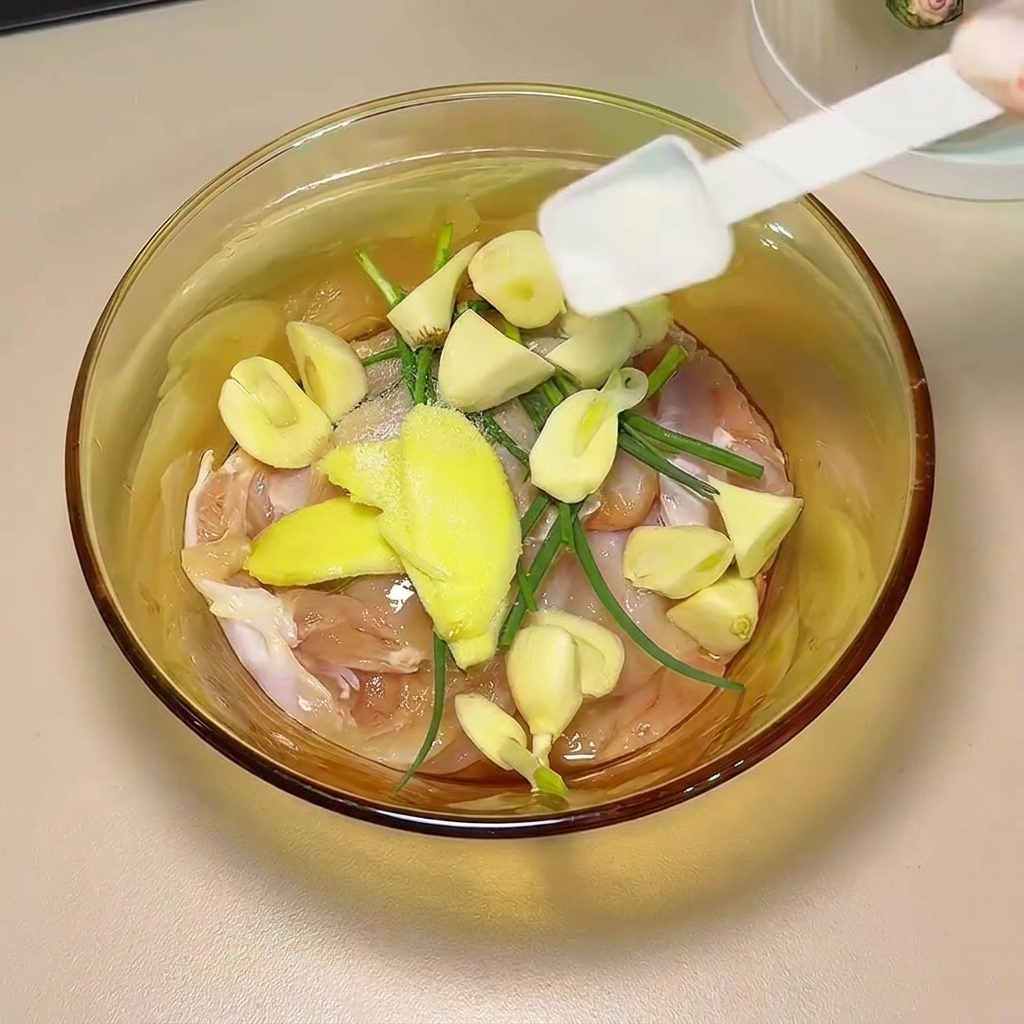 Soy sauce and spices being poured over the chicken thighs and aromatics in a glass bowl.