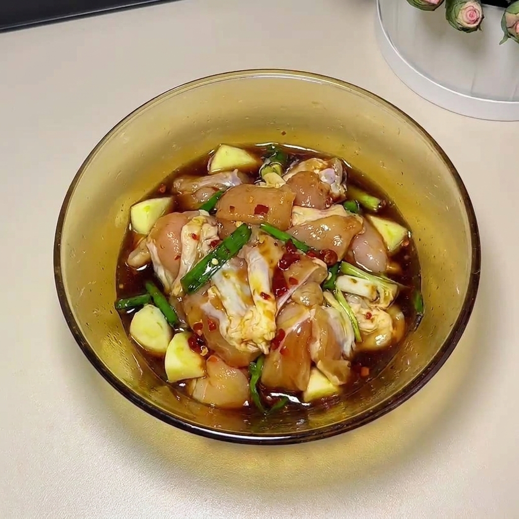 Raw chicken thighs being massaged by hand with marinade ingredients in a glass bowl.